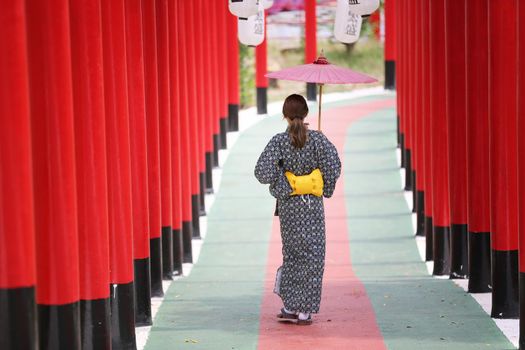 woman in kimono holding umbrella walking into at the shrine red gate, in Japanese garden.