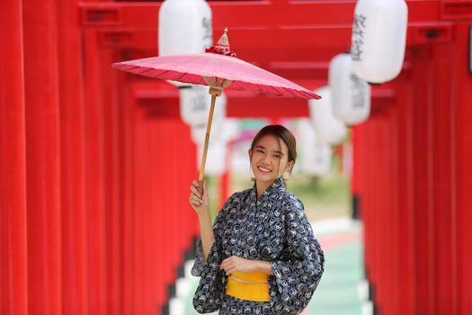 woman in kimono holding umbrella walking into at the shrine red gate, in Japanese garden.