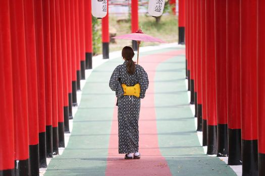 woman in kimono holding umbrella walking into at the shrine red gate, in Japanese garden.