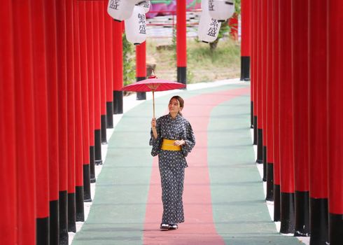 woman in kimono holding umbrella walking into at the shrine red gate, in Japanese garden.