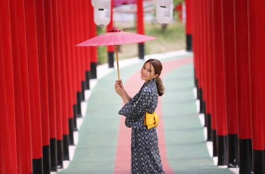 woman in kimono holding umbrella walking into at the shrine red gate, in Japanese garden.