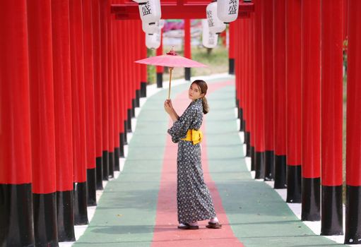 woman in kimono holding umbrella walking into at the shrine red gate, in Japanese garden.