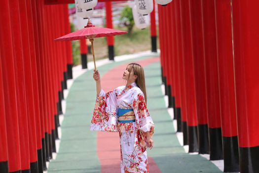 woman in kimono holding umbrella walking into at the shrine red gate, in Japanese garden.