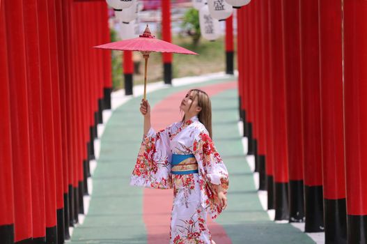 woman in kimono holding umbrella walking into at the shrine red gate, in Japanese garden.
