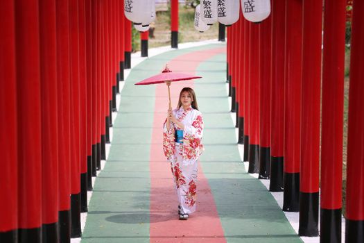 woman in kimono holding umbrella walking into at the shrine red gate, in Japanese garden.
