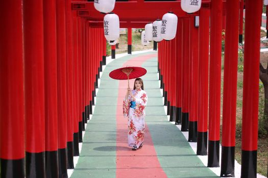 woman in kimono holding umbrella walking into at the shrine red gate, in Japanese garden.
