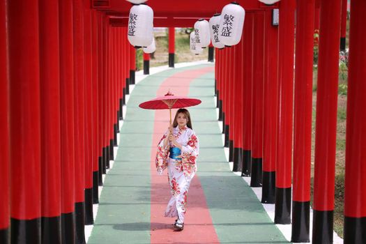 woman in kimono holding umbrella walking into at the shrine red gate, in Japanese garden.