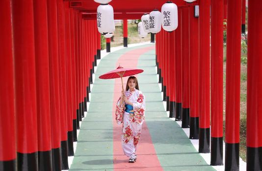 woman in kimono holding umbrella walking into at the shrine red gate, in Japanese garden.