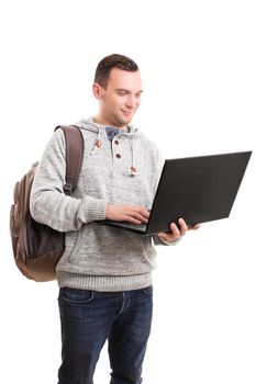 Portrait of a young male student with a backpack holding a laptop computer, isolated on white background. Young guy in casual clothing and backpack holding and using open laptop.