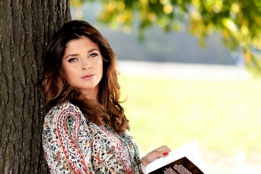 Portrait of a sensual and lovely woman with nice hairstyle reading book outdoor on a sunny day under the tree ( copy space)