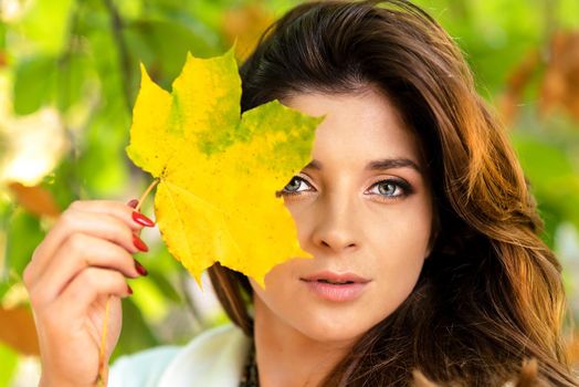 Portrait of a beautiful and lovely young woman holding fallen leaf and posing in the park on a sunny day.