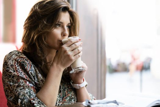 Beautiful and elegant young woman drinking coffee in a restaurant and is thoughtful while reading a book.