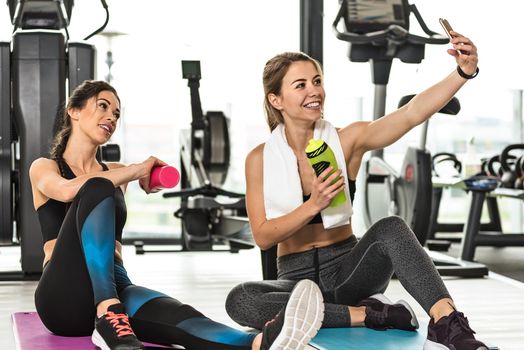 Two cute girls taking a selfie photo while doing training at the gym