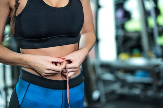 Healthy lifestyle concept - woman after workout at the gym measures her perfect waistline with a measuring tape in close-up