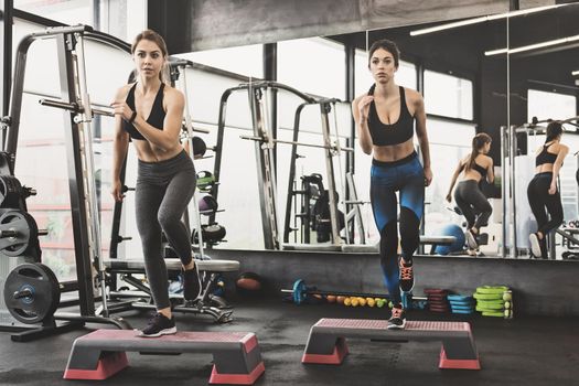 Two fit attractive women doing workout with steppers in the gym