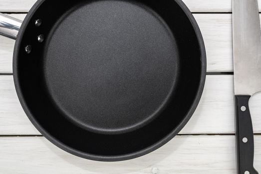 Culinary template - top view of an empty pan and kitchen knife on a white wooden table. 