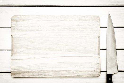 Rustic culinary template - top view of an empty cutting board and knife on a white wooden table.