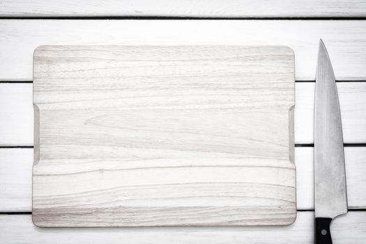 Rustic culinary template - top view of an empty cutting board and knife on a white wooden table.