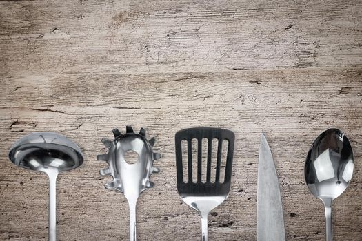 Top view of a silver kitchen utensil collection on a wooden old plank with copy space.