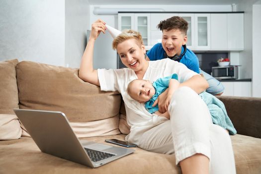 Smiling young woman with her two sons sitting on couch and having video chat on wireless laptop. Happy family using technology at home.