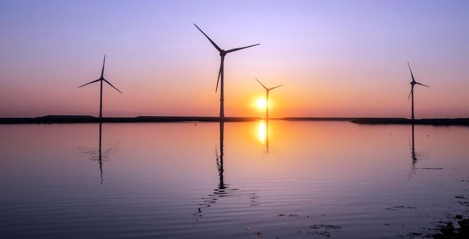 wind turbines and colorful sunrise reflected in water on work island neeltje jans in dutch province of zeeland