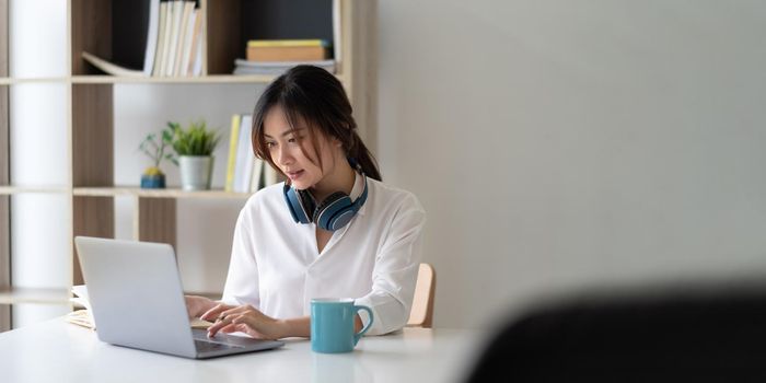 Portrait of a pretty young asian woman studying online with laptop computer while sitting at the table and notebook at home