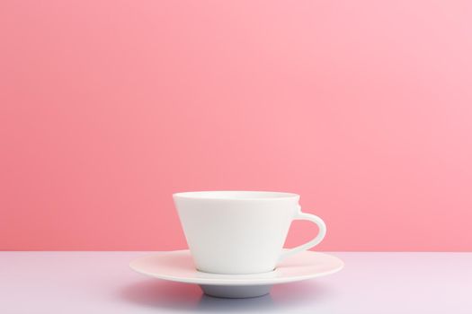 White ceramic coffee cup with saucer on white table against light pink background with copy space. Concept of hot drinks and kitchen utensil