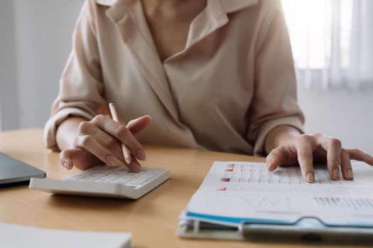 Close up of businesswoman or accountant hand holding pencil working on calculator to calculate financial data report, accountancy document and laptop computer at office, business concept
