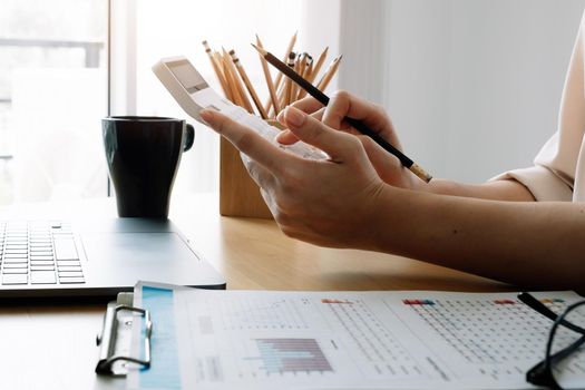 Close up of businesswoman or accountant hand holding pencil working on calculator to calculate financial data report, accountancy document and laptop computer at office, business concept