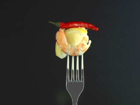 Shrimp on a fork. Prawn meat boiled on a fork with lemon t red pepper on a black background. High quality photo