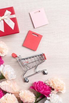 Design concept of Mother's Day greeting with carnation flower, holiday gift idea and shopping cart on wooden background.