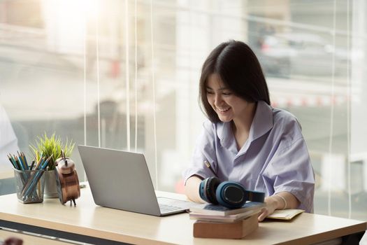 Online education. Asian girl with headphones makes an online lesson using a computer video call to a virtual teacher at home.