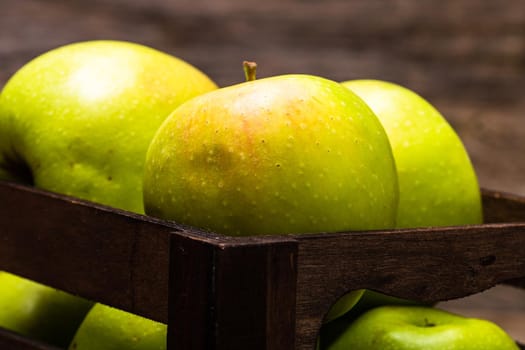 Wooden crate with ripe green apples on wooden table.