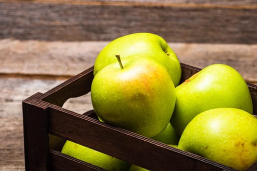 Wooden crate with ripe green apples on wooden table.