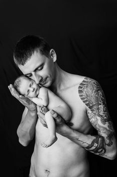 Father with tattoo on his arm is holding his newborn baby boy on a black and white background. High quality photo