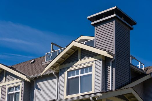 Window on upper level of residential building. Low rise building with patio on the roof on blue sky background