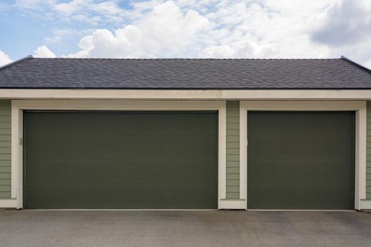 Three car garage with wide double door on cloudy sky background
