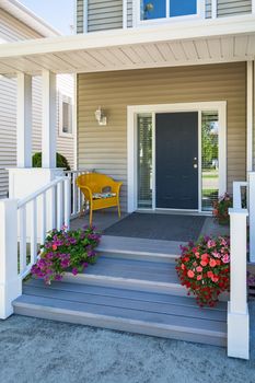 Family house entrance with yellow chair under the porch and decorative blossoming flowers