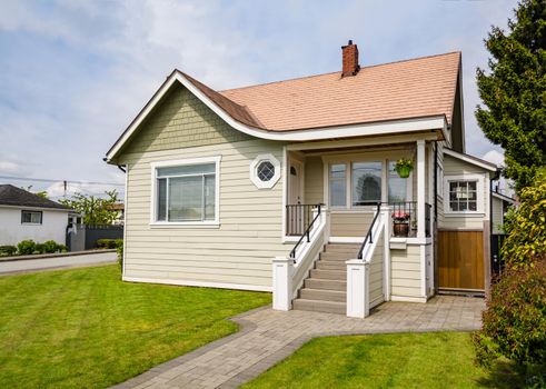 Small residential house with neat green lawn on front yard. Family house with concrete pathway over front yard