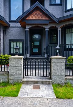 Porch and entrance of residential house with metal grid gate in front. Dark colored house with entrance gate