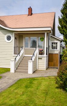 Main entrance of small residential house with paved walkway over green lawn of front yard. Family house with doorsteps to the entrance under the porch