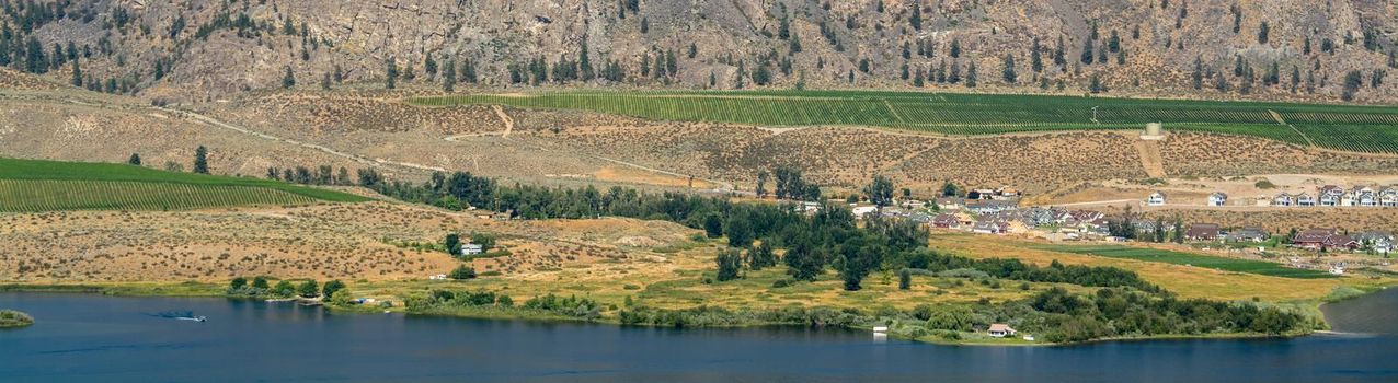 Okanagan valley panoramic view with residential area and orchard farm fields. Residential houses in Okanagan valley built on Osoyoos lake shore with mountains on the background