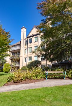 Low rise residential building and wooden bench in front. Apartment building and small park area on sunny day
