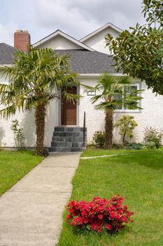 Concrete pathway to the house entrance over front yard decorated with red flowers