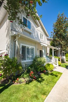 Facade of family house with blue chair under the porch and decorative blossoming flowers in front
