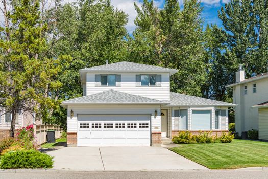 A perfect neighbourhood. Family house with landscaped front yard and concrete driveway. Residential house with wide garage on sunny day in British Columbia