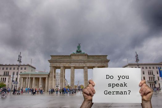 a man holding a sign with the Brandenburg Gate in Berlin in the background
