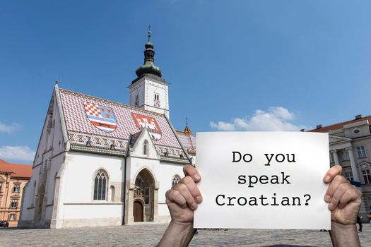 a man holding a sign with the St. Mark's church in the center of Zagreb in the background