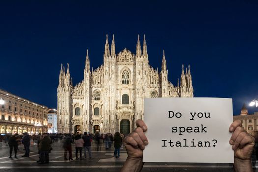 a man holding a sign with the night view of Milan cathedral in the background