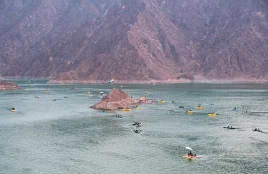 BEAUTIFUL AERIAL VIEW OF THE PADDLE BOATS, KAYAKS IN THE HATTA WATER DAM ON A CLOUDY DAY AT SUNSET TIME IN THE MOUNTAINS ENCLAVE REGION OF DUBAI, UNITED ARAB EMIRATES.